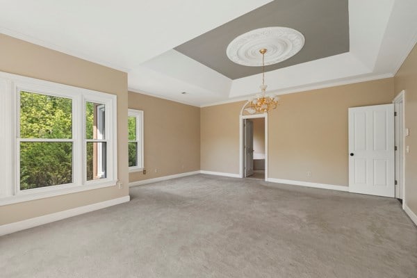 carpeted spare room featuring a raised ceiling, a notable chandelier, and crown molding