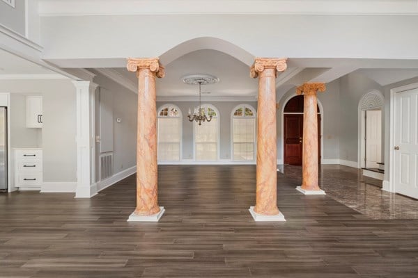 interior space featuring ornate columns, dark hardwood / wood-style flooring, a notable chandelier, and ornamental molding