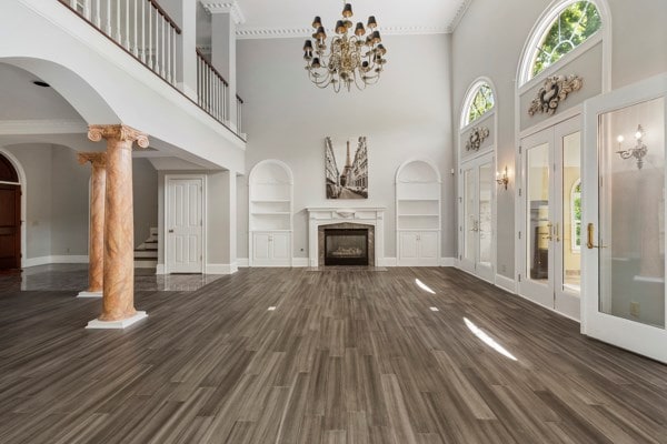 unfurnished living room with a high end fireplace, french doors, built in shelves, a towering ceiling, and decorative columns