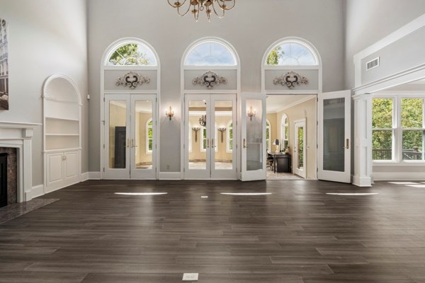 unfurnished living room with a high ceiling, an inviting chandelier, french doors, dark hardwood / wood-style floors, and a premium fireplace