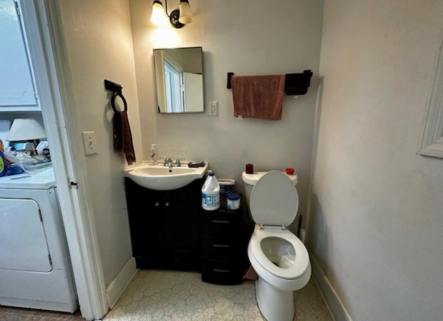 half bathroom with washer / clothes dryer, vanity, toilet, and baseboards