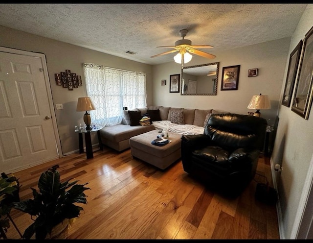 living room featuring baseboards, visible vents, light wood-style flooring, ceiling fan, and a textured ceiling