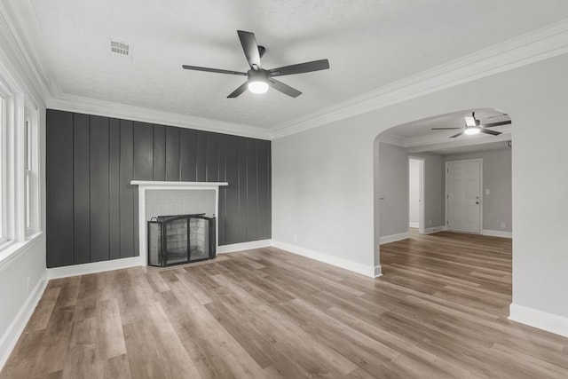 unfurnished living room featuring a fireplace, light wood-type flooring, ceiling fan, and crown molding