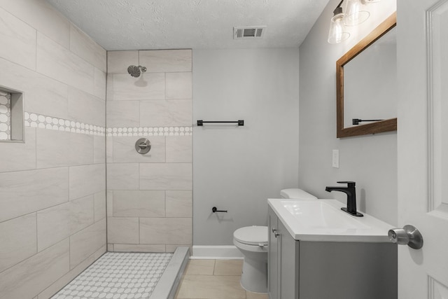 bathroom featuring vanity, tile patterned flooring, toilet, a textured ceiling, and a tile shower