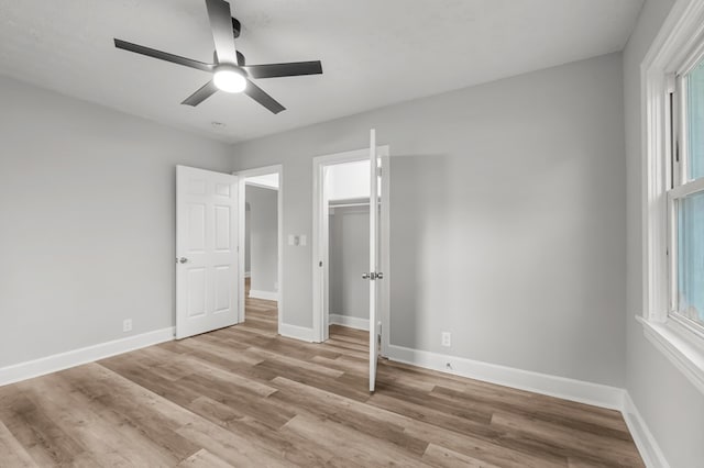 unfurnished bedroom featuring ceiling fan, a closet, light hardwood / wood-style floors, and a spacious closet