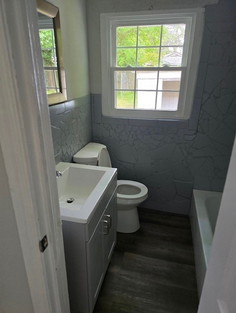 bathroom with hardwood / wood-style flooring, tile walls, vanity, a tub, and toilet