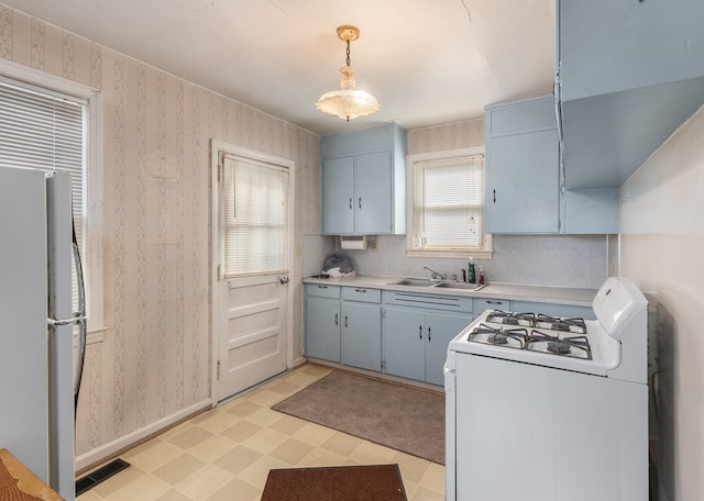 kitchen with a sink, white appliances, light floors, and wallpapered walls