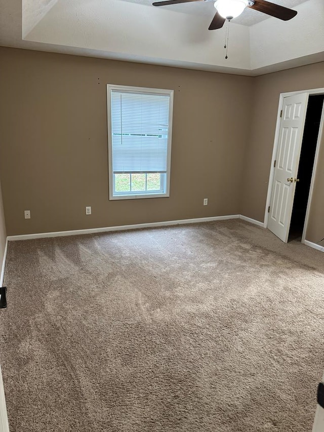 unfurnished room with a raised ceiling, carpet, and ceiling fan