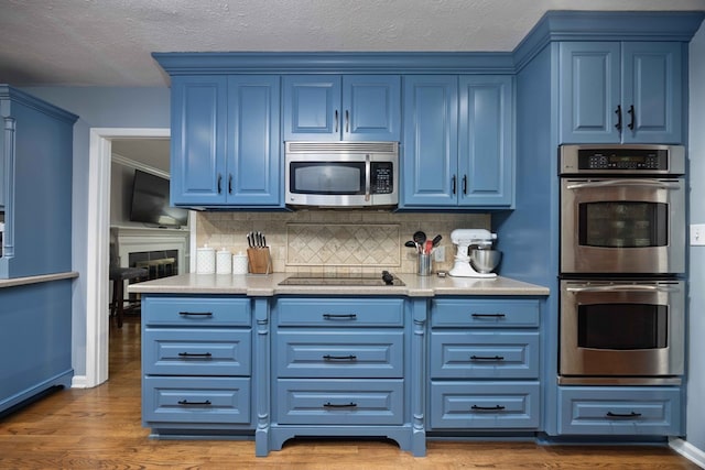 kitchen with blue cabinetry, backsplash, wood finished floors, and appliances with stainless steel finishes