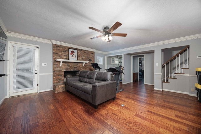 living area featuring stairway, wood finished floors, ceiling fan, a textured ceiling, and a brick fireplace