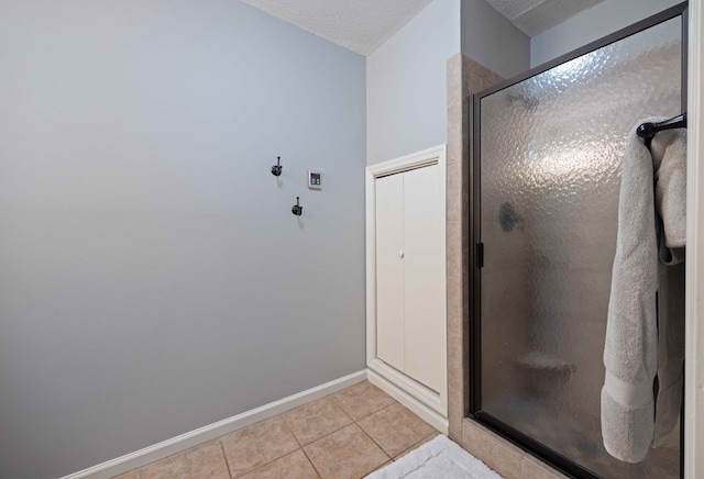 bathroom featuring tile patterned flooring, a stall shower, a textured ceiling, and baseboards