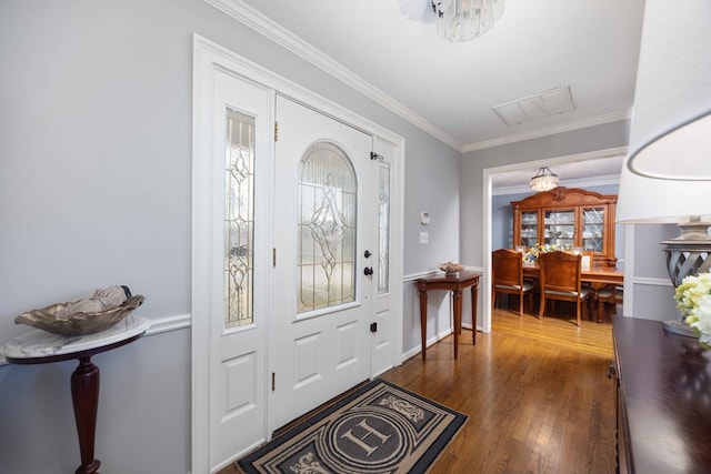 entrance foyer with a chandelier, visible vents, ornamental molding, and wood finished floors