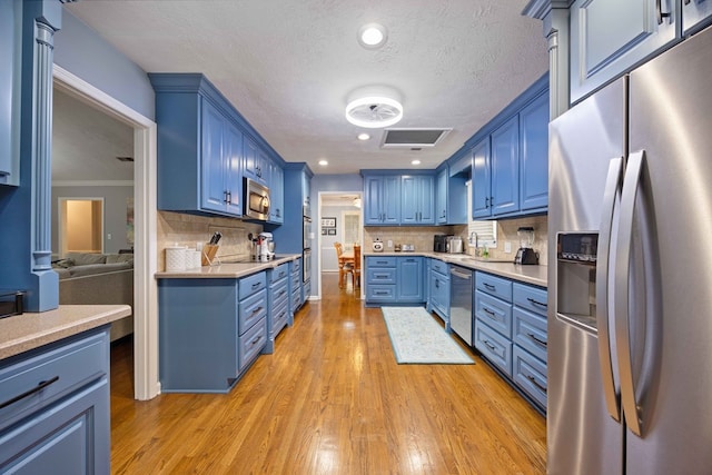 kitchen with light countertops, blue cabinets, light wood-type flooring, and stainless steel appliances