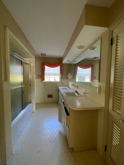 bathroom with tile patterned floors, vanity, enclosed tub / shower combo, and tile walls