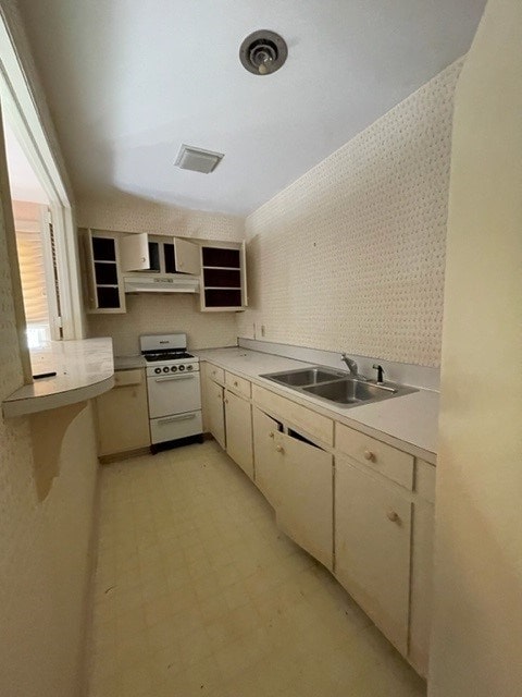 kitchen featuring ventilation hood, sink, white gas range oven, and cream cabinets