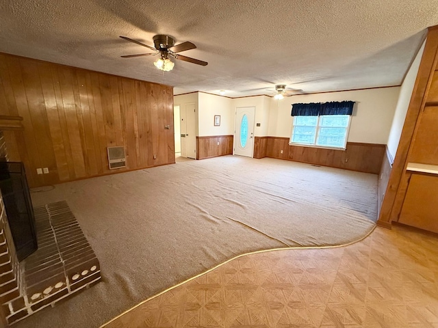 interior space with ceiling fan, heating unit, a textured ceiling, wooden walls, and a fireplace