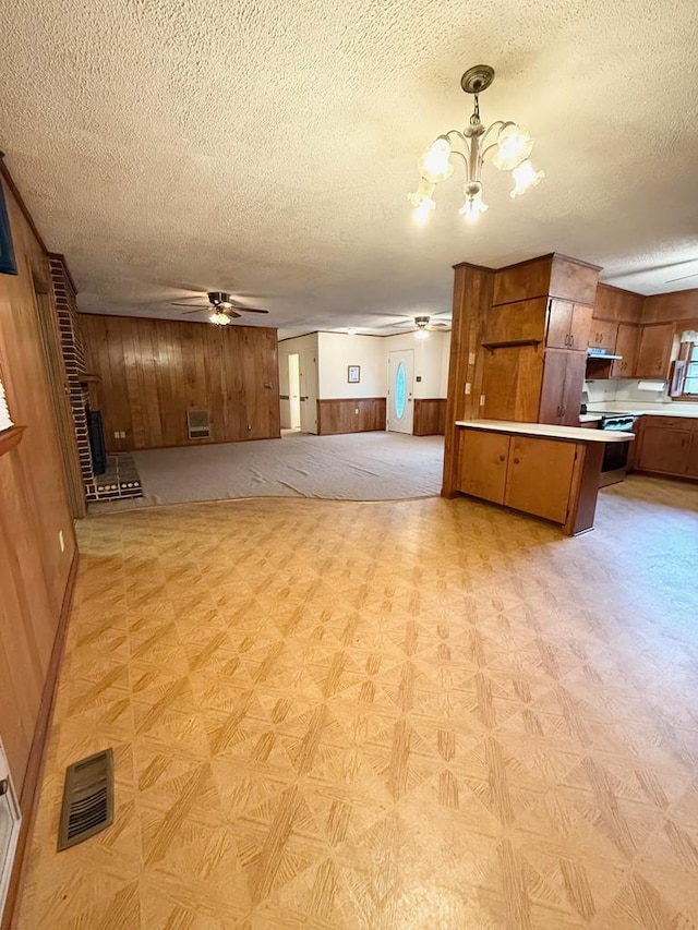 kitchen featuring pendant lighting, ceiling fan with notable chandelier, wooden walls, a textured ceiling, and kitchen peninsula