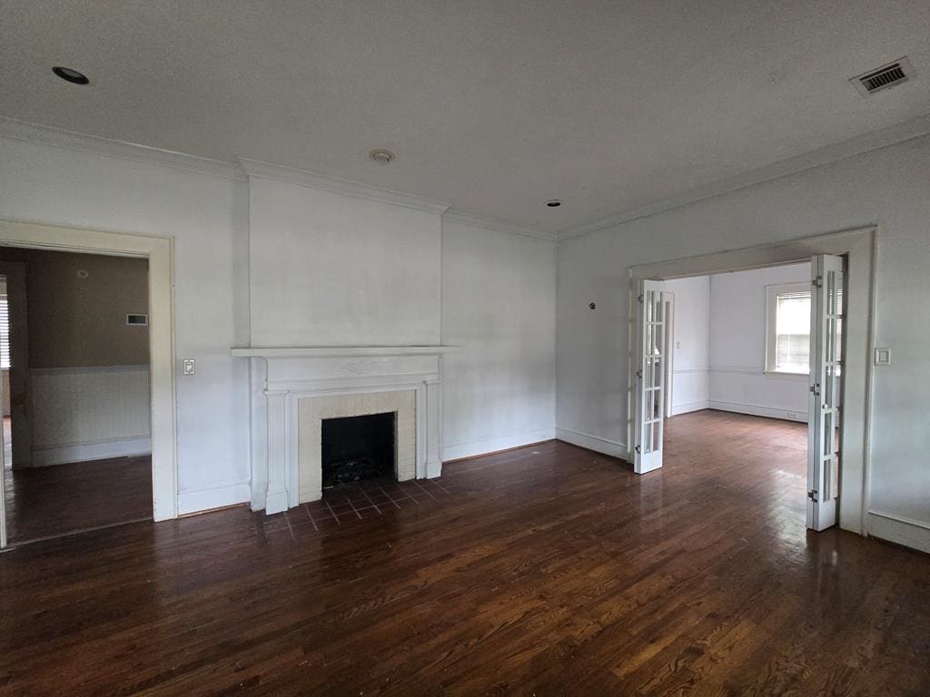 unfurnished living room with a fireplace, baseboards, wood finished floors, visible vents, and ornamental molding