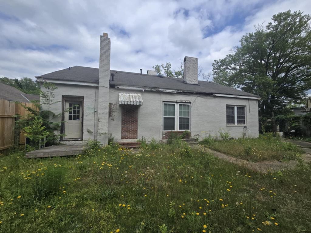 back of property featuring fence, a chimney, and brick siding
