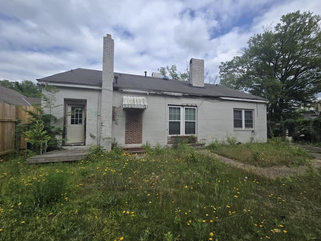back of property featuring fence, a chimney, and brick siding