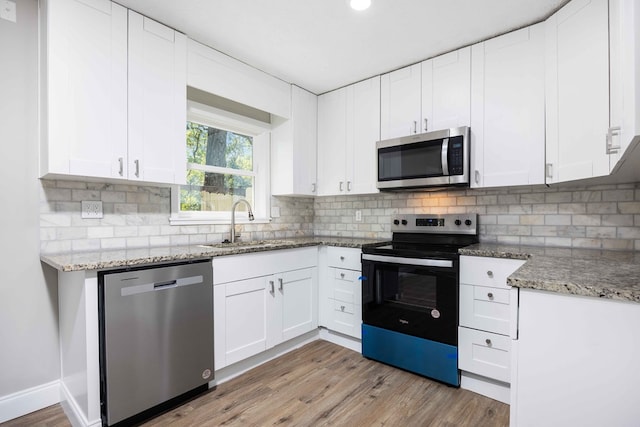 kitchen featuring white cabinetry, sink, stainless steel appliances, tasteful backsplash, and light wood-type flooring