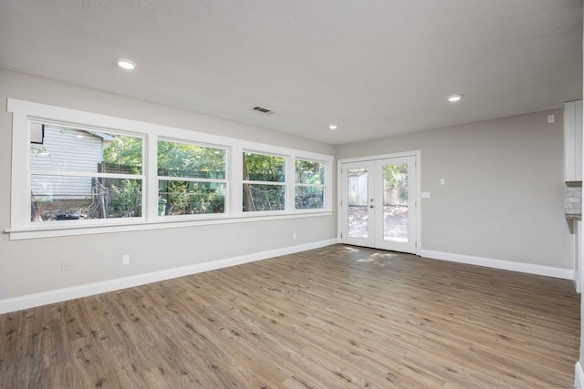 unfurnished room with light hardwood / wood-style floors, a textured ceiling, and french doors