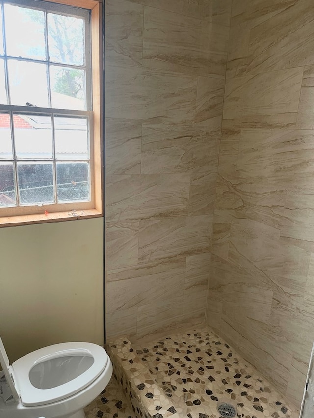 bathroom featuring toilet, a healthy amount of sunlight, and a tile shower