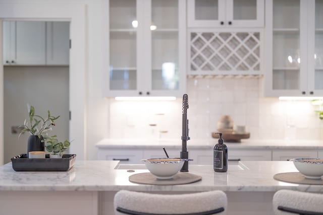 interior space with white cabinets, decorative backsplash, and light stone counters