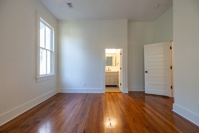 unfurnished bedroom with connected bathroom, multiple windows, and dark wood-type flooring