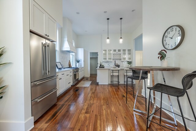 kitchen with dark wood-type flooring, a kitchen bar, high quality appliances, white cabinets, and custom range hood