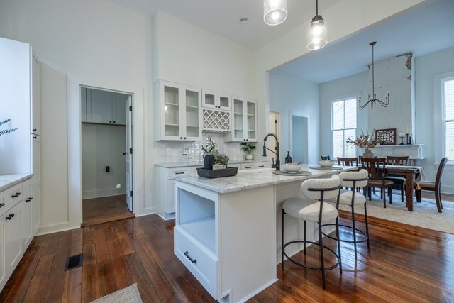 kitchen featuring light stone countertops, hanging light fixtures, dark hardwood / wood-style floors, an island with sink, and white cabinets