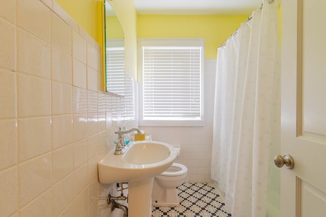 bathroom featuring toilet, a sink, and tile walls