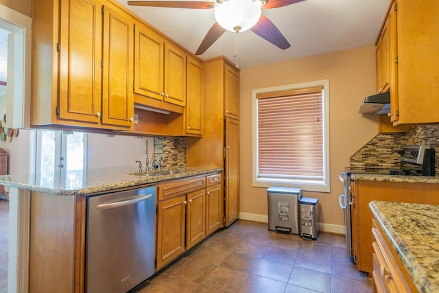 kitchen featuring under cabinet range hood, light stone counters, stainless steel appliances, and a sink