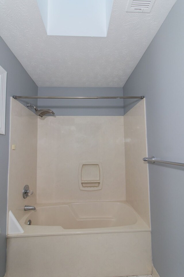 bathroom with bathtub / shower combination, a textured ceiling, and a skylight