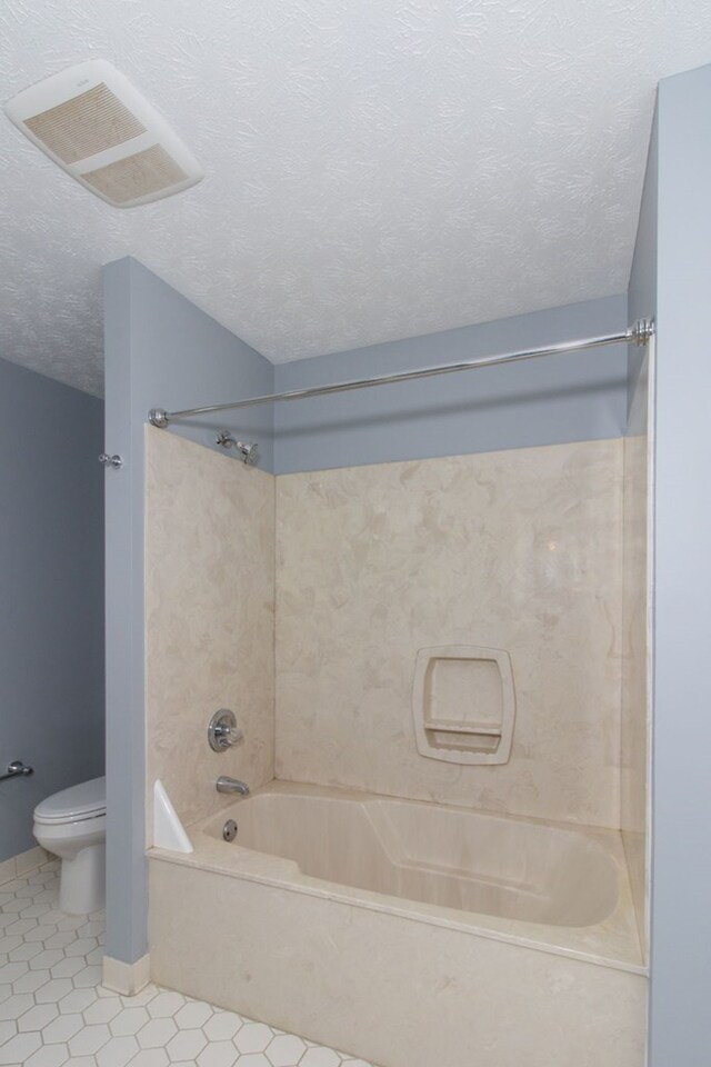 bathroom with tile patterned flooring, tiled shower / bath combo, toilet, and a textured ceiling