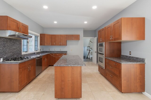 kitchen with light tile patterned flooring, ventilation hood, dark stone countertops, appliances with stainless steel finishes, and a kitchen island