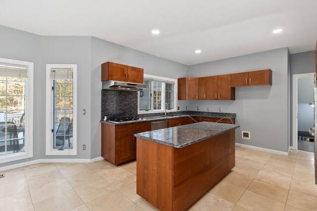 kitchen with appliances with stainless steel finishes, dark stone counters, sink, exhaust hood, and a center island