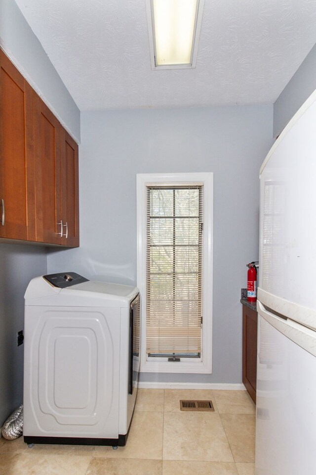 laundry room featuring light tile patterned flooring, cabinets, a textured ceiling, and independent washer and dryer