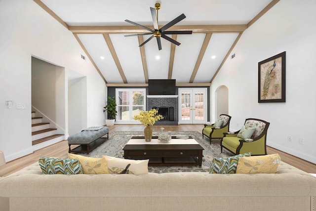 living room with stairs, a fireplace, beamed ceiling, and wood finished floors