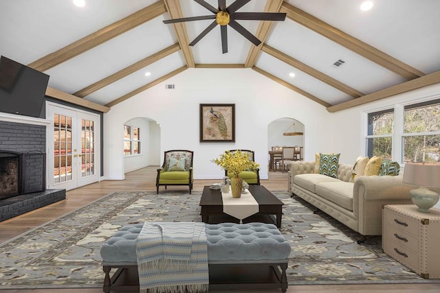 living area with visible vents, arched walkways, wood finished floors, a fireplace, and beam ceiling