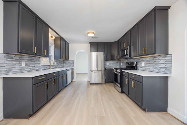 kitchen with arched walkways, light countertops, visible vents, light wood-style flooring, and appliances with stainless steel finishes