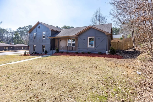 split level home with covered porch, a shingled roof, fence, and a front yard