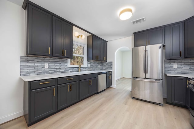 kitchen with arched walkways, stainless steel appliances, visible vents, light wood-style floors, and light countertops