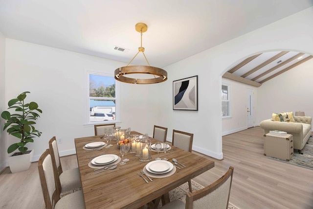 dining area with arched walkways, lofted ceiling with beams, light wood-style flooring, visible vents, and baseboards