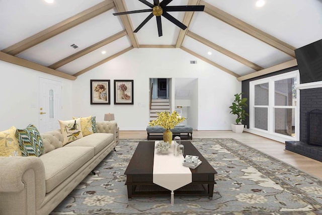 living area with lofted ceiling with beams, wood finished floors, visible vents, stairs, and a brick fireplace