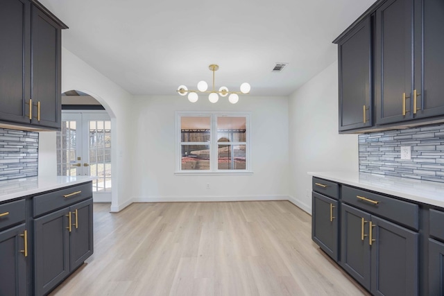 kitchen with arched walkways, visible vents, light countertops, light wood finished floors, and tasteful backsplash