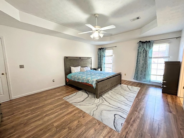 bedroom featuring hardwood / wood-style floors, ceiling fan, a tray ceiling, and multiple windows