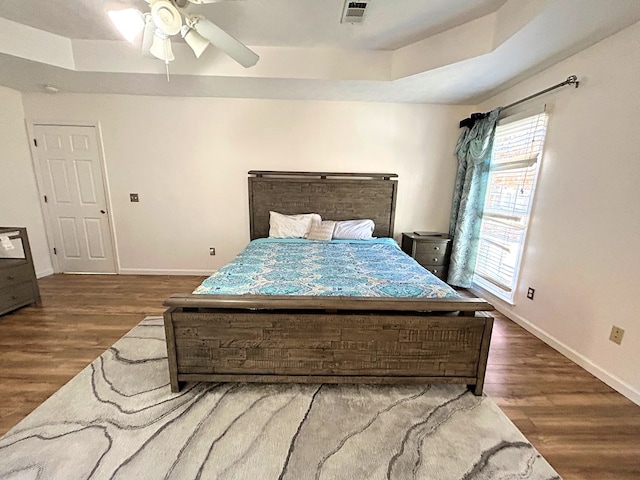 bedroom featuring dark hardwood / wood-style floors, ceiling fan, and a raised ceiling