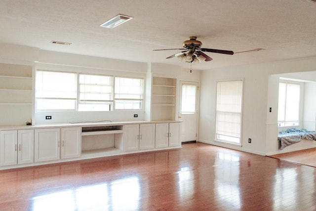 unfurnished living room with ceiling fan, built in desk, and light hardwood / wood-style floors