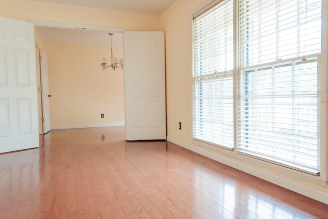 empty room featuring a notable chandelier and light wood-type flooring